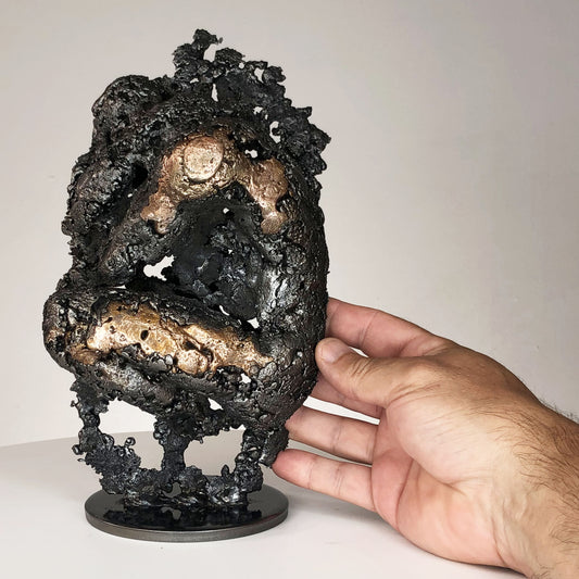 Sculpture de Philippe Buil représentant un corps d'homme accroupi intégré à une forme évoquant une montagne. Sculpture en dentelle de métal : acier et bronze.