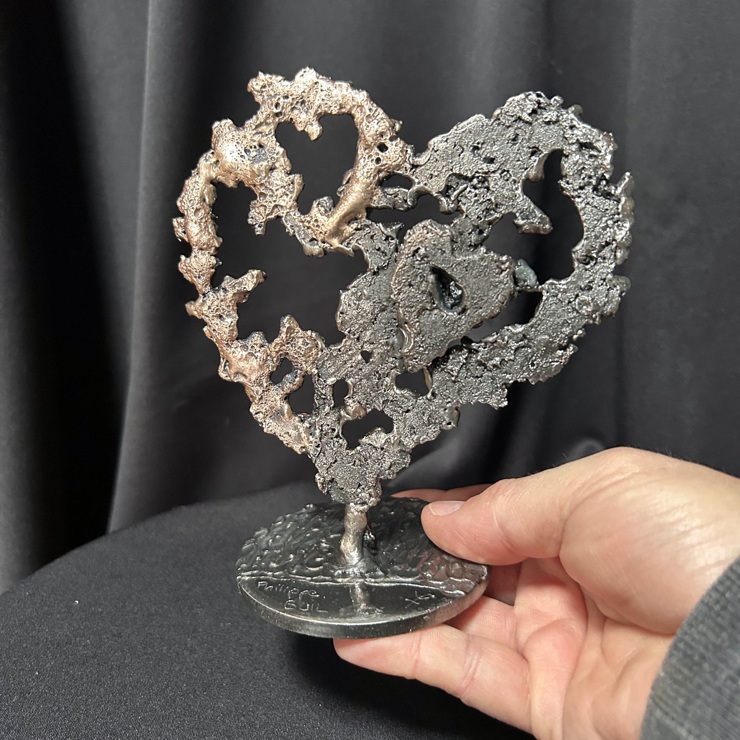 main de l'artiste présentant son coeur sculpté en dentelle de métal acier et bronze