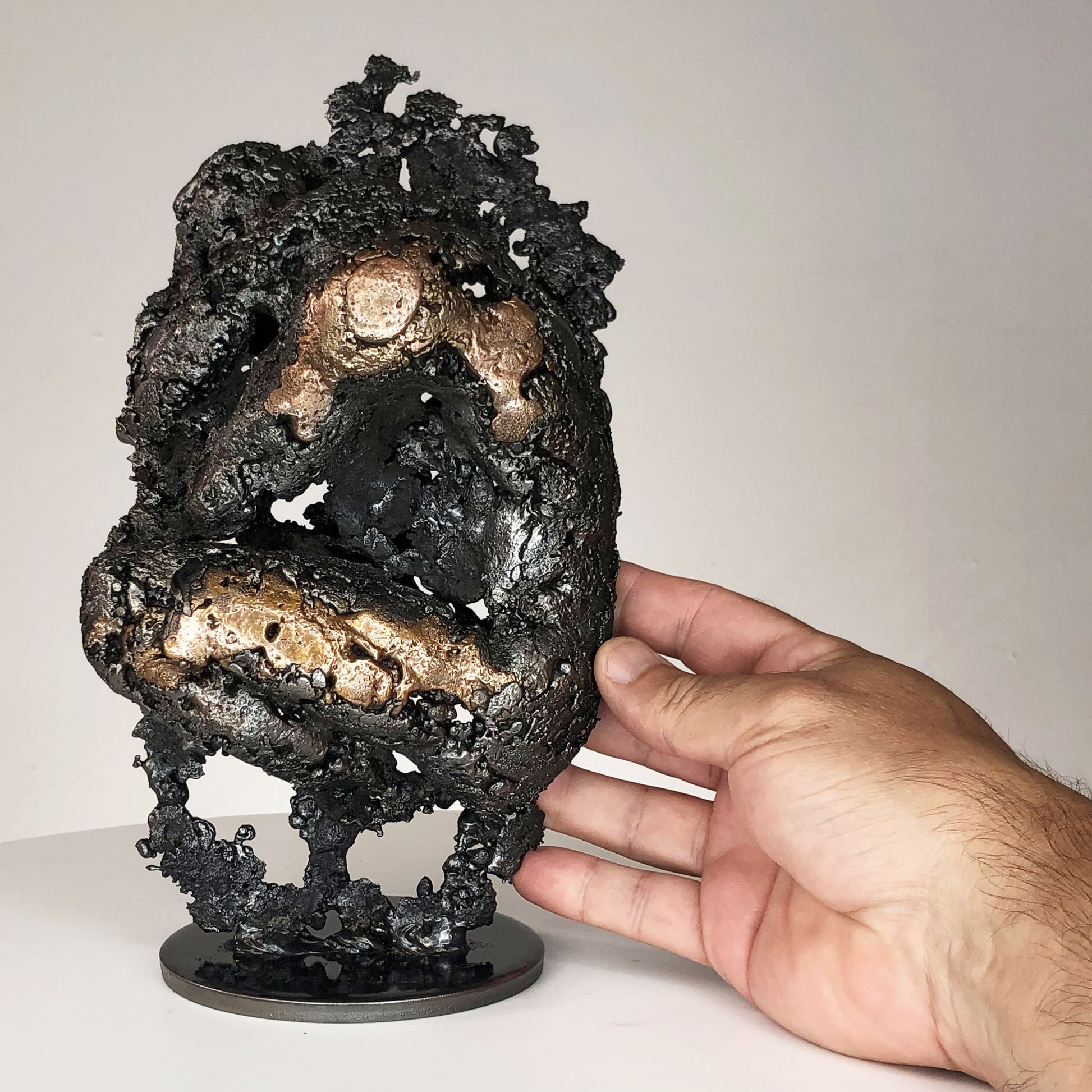 Sculpture de Philippe Buil représentant un corps d'homme accroupi intégré à une forme évoquant une montagne. Sculpture en dentelle de métal : acier et bronze.