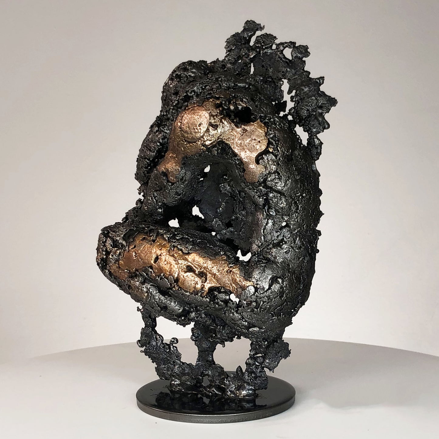 Sculpture de Philippe Buil représentant un corps d'homme accroupi intégré à une forme évoquant une montagne. Sculpture en dentelle de métal : acier et bronze.