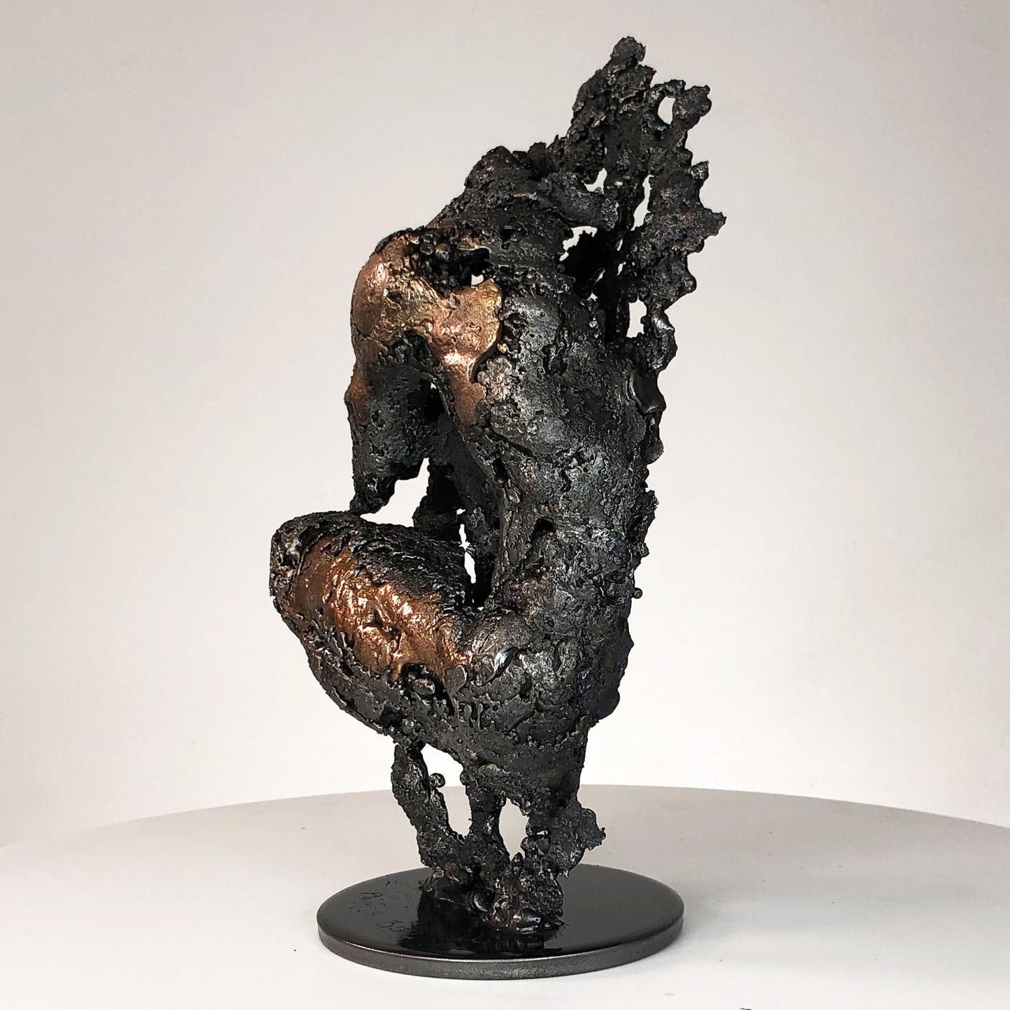 Sculpture de Philippe Buil représentant un corps d'homme accroupi intégré à une forme évoquant une montagne. Sculpture en dentelle de métal : acier et bronze.