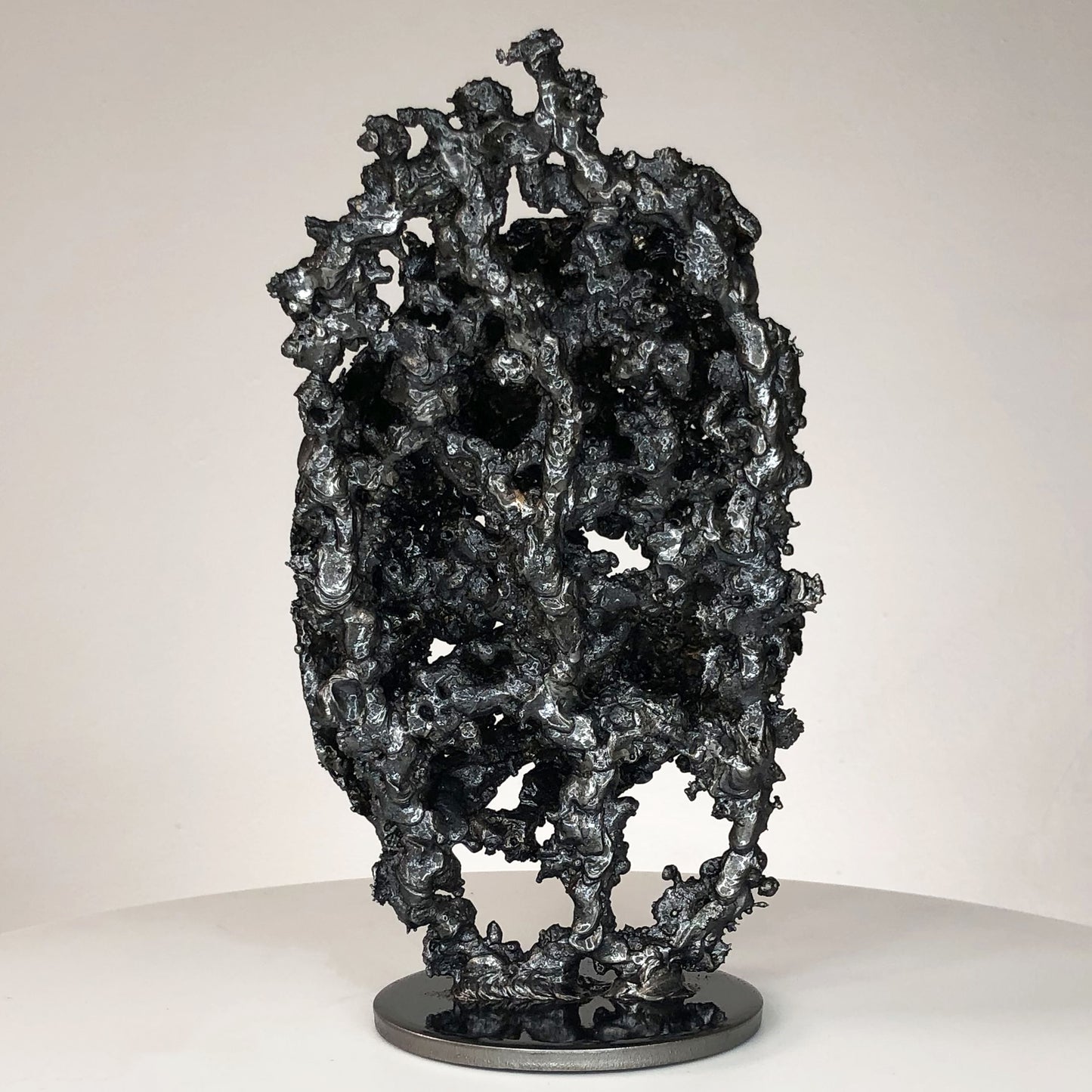 Sculpture de Philippe Buil représentant un corps d'homme accroupi intégré à une forme évoquant une montagne. Sculpture en dentelle de métal : acier et bronze.