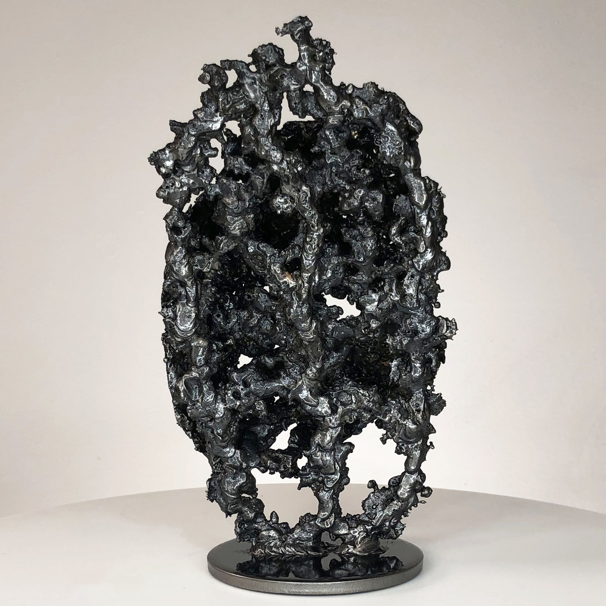 Sculpture de Philippe Buil représentant un corps d'homme accroupi intégré à une forme évoquant une montagne. Sculpture en dentelle de métal : acier et bronze.