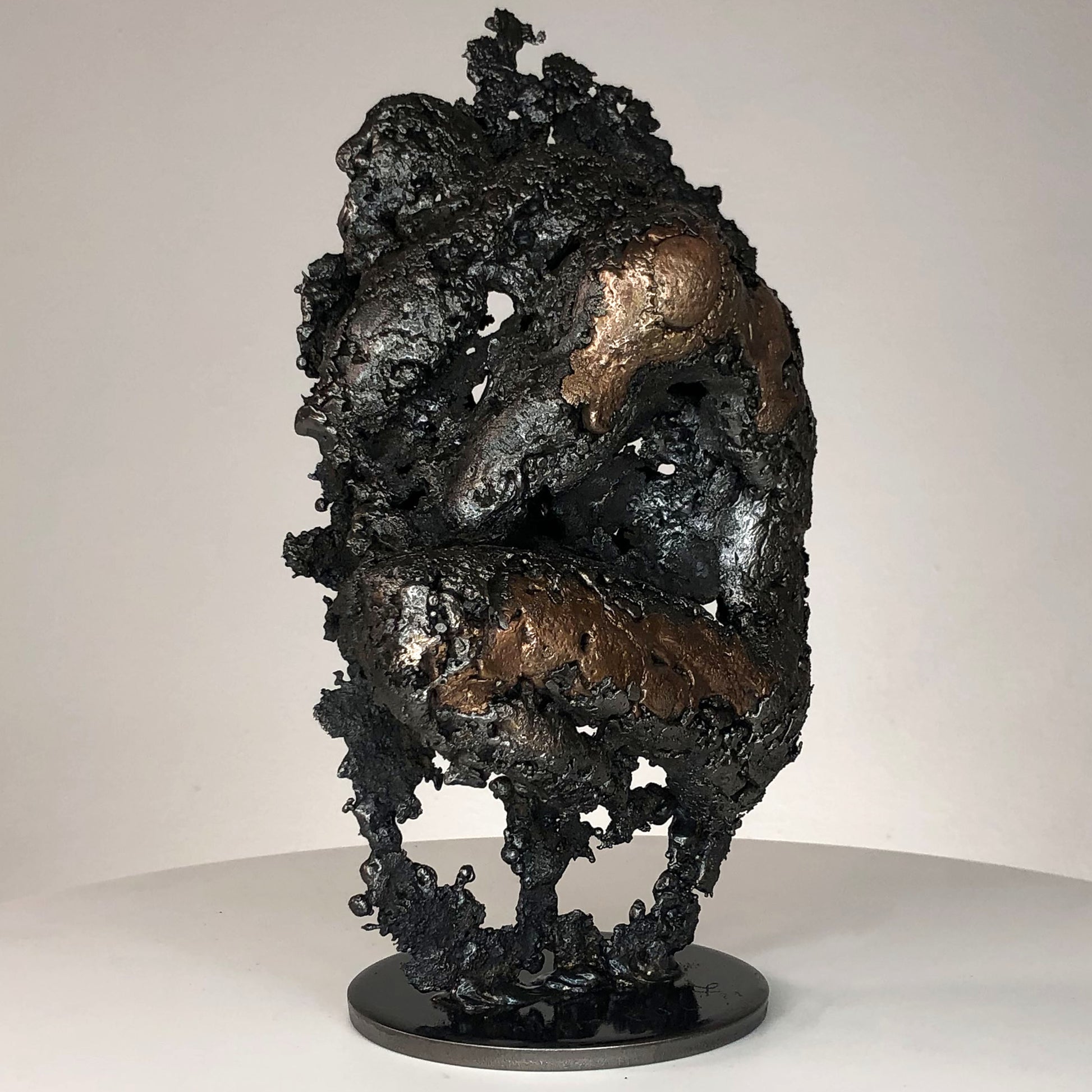 Sculpture de Philippe Buil représentant un corps d'homme accroupi intégré à une forme évoquant une montagne. Sculpture en dentelle de métal : acier et bronze.