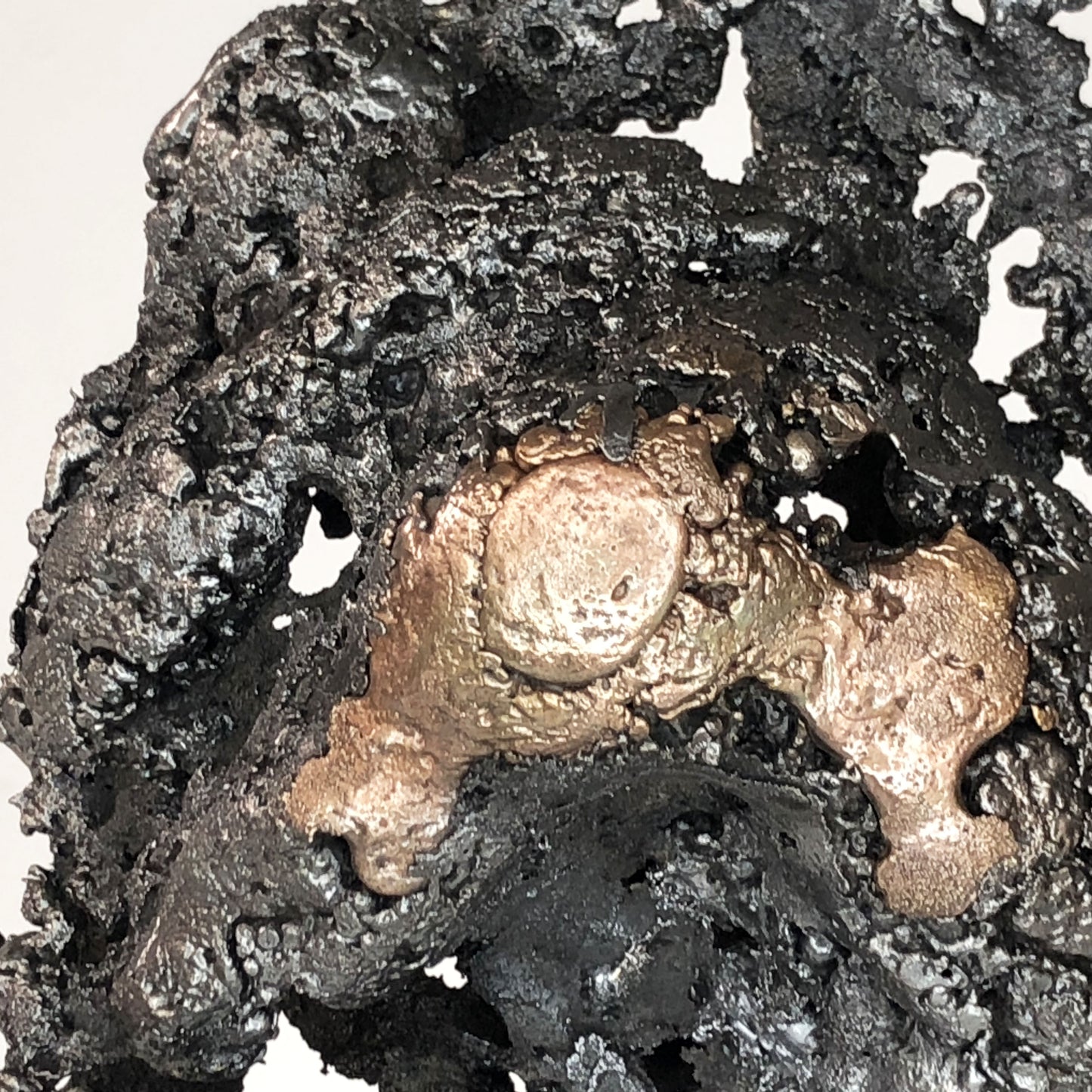 Sculpture de Philippe Buil représentant un corps d'homme accroupi intégré à une forme évoquant une montagne. Sculpture en dentelle de métal : acier et bronze.