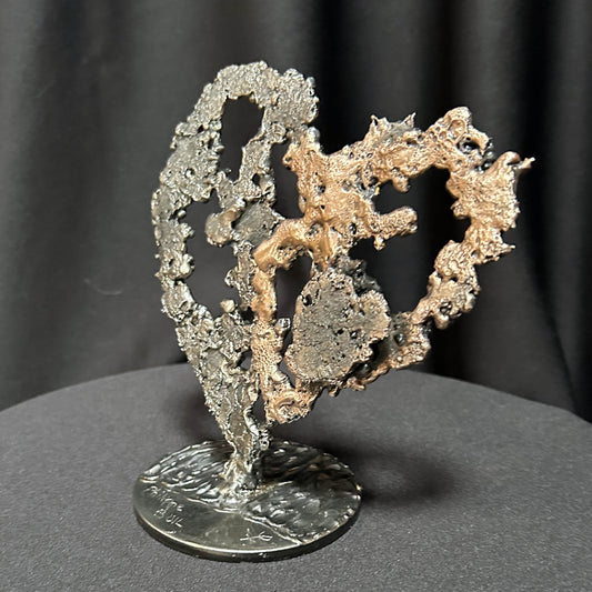 Sculpture de cœur en dentelle de métal noir et bronze par Philippe Buil, vue de profil sur socle circulaire.