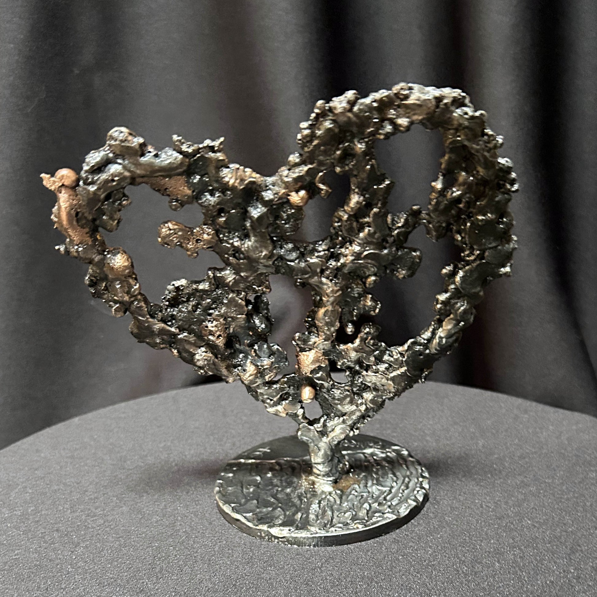 Sculpture de cœur en dentelle de métal noir et bronze par Philippe Buil, vue de dos sur socle circulaire.