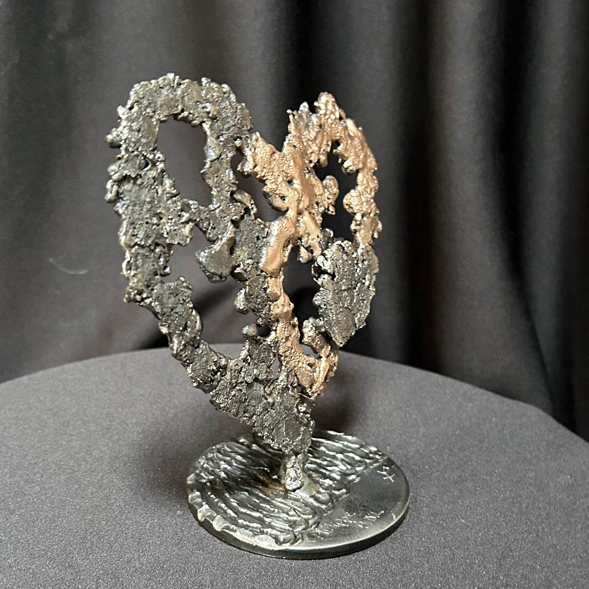 Sculpture de cœur en dentelle de métal noir et bronze par Philippe Buil, vue de profil sur socle circulaire.
