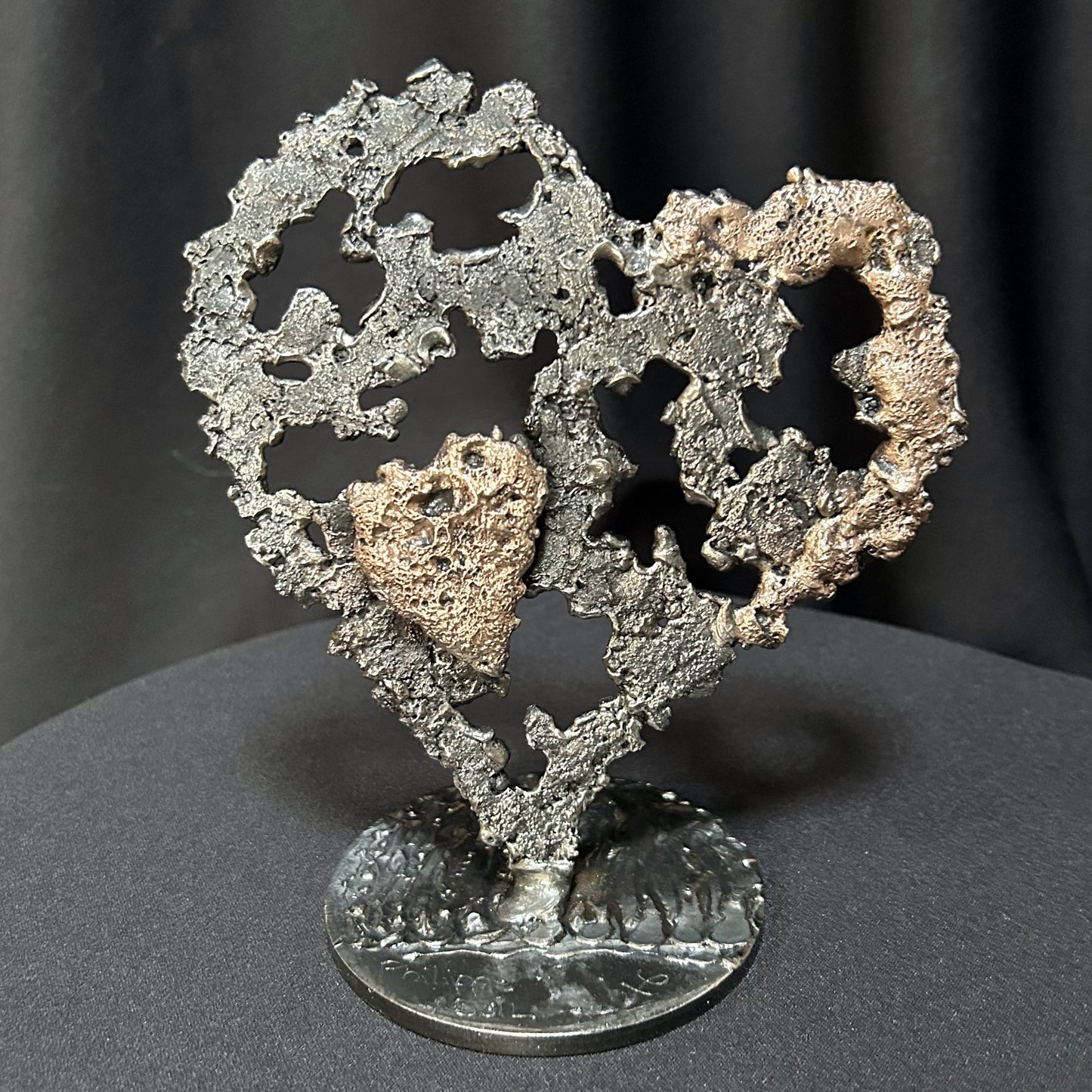 Sculpture en métal de Philippe Buil représentant un grand cœur ajouré en dentelle d'acier gris avec des reflets de bronze, contenant en son centre un petit cœur plein en bronze doré.