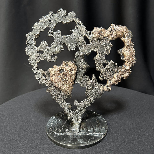 Sculpture en métal de Philippe Buil représentant un grand cœur ajouré en dentelle d'acier gris avec des reflets de bronze, contenant en son centre un petit cœur plein en bronze doré.