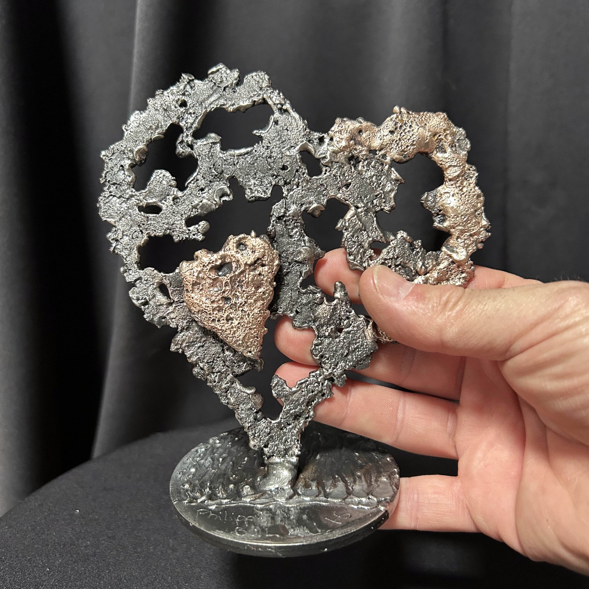 main de l'artiste tenant sa sculpture en forme de coeur en dentelle d'acier et de bronze