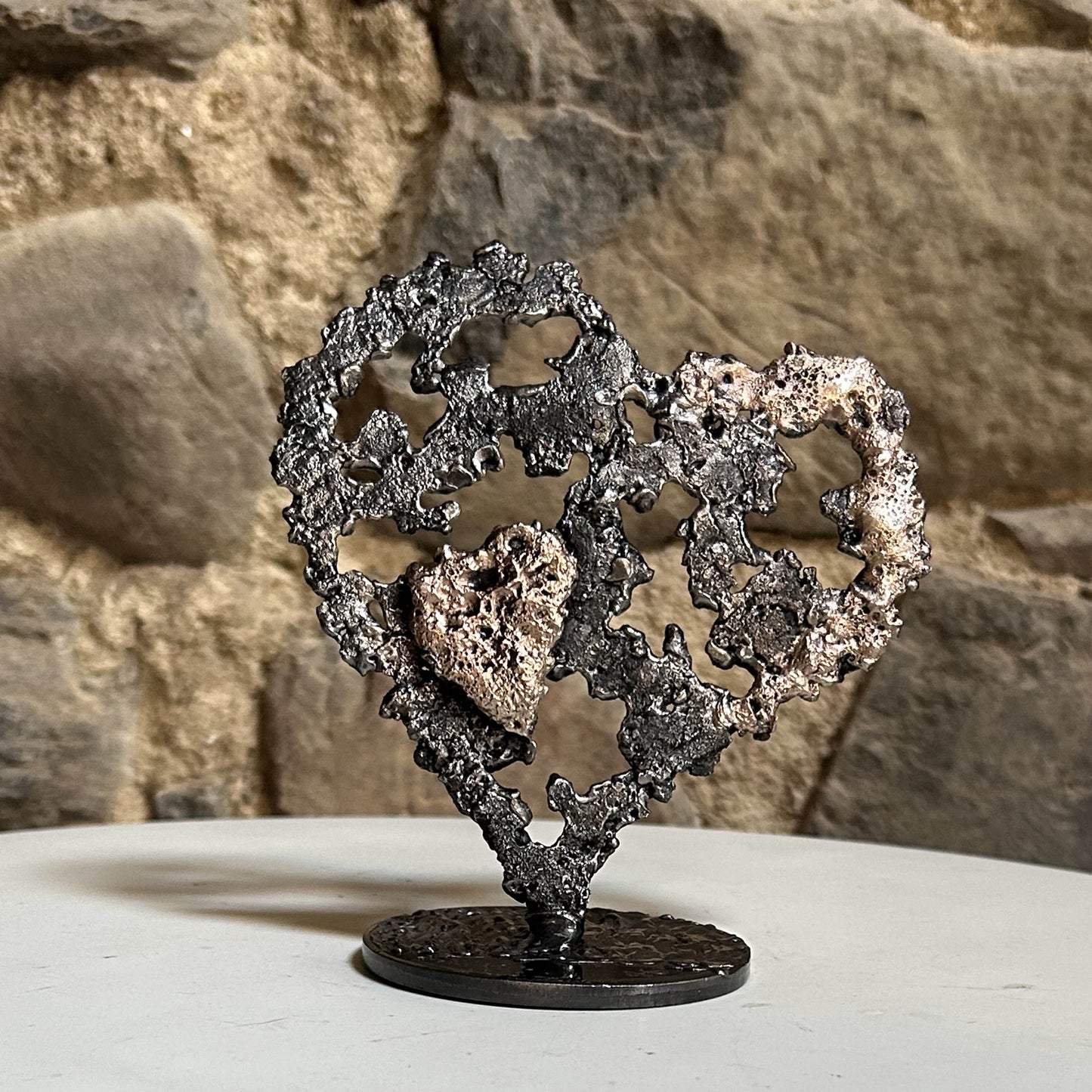 Sculpture coeur en acier et bronze - Dentelle de métal de Philippe Buil sur mur en pierre