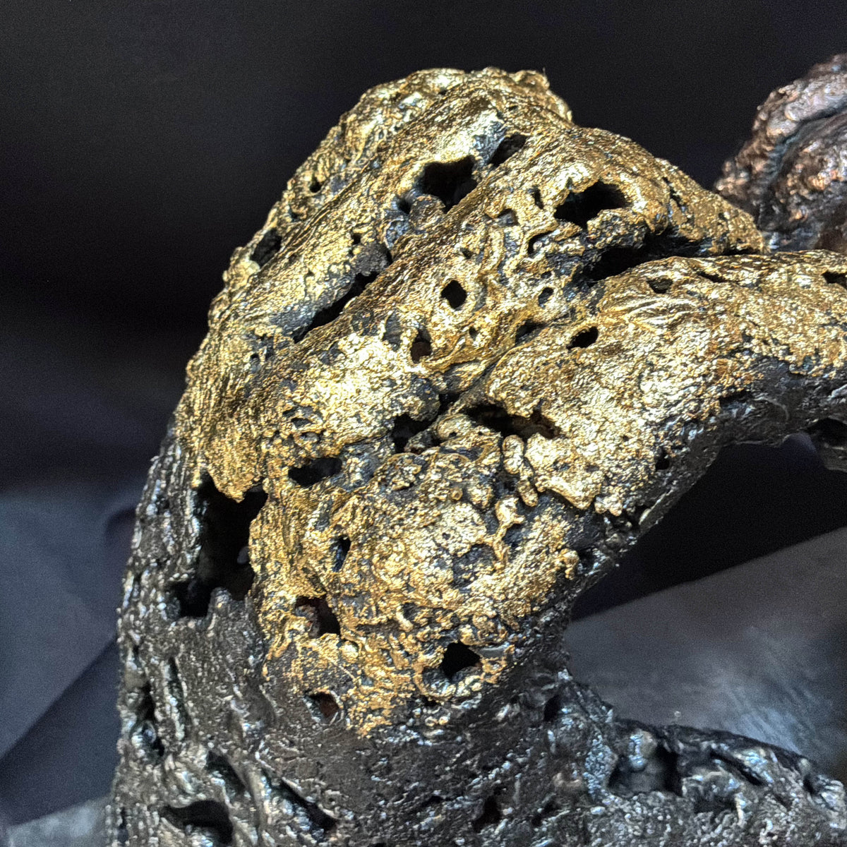 Gros plan sur la finition à la feuille d’or 24 carats de la main gauche de la sculpture « Un échange »