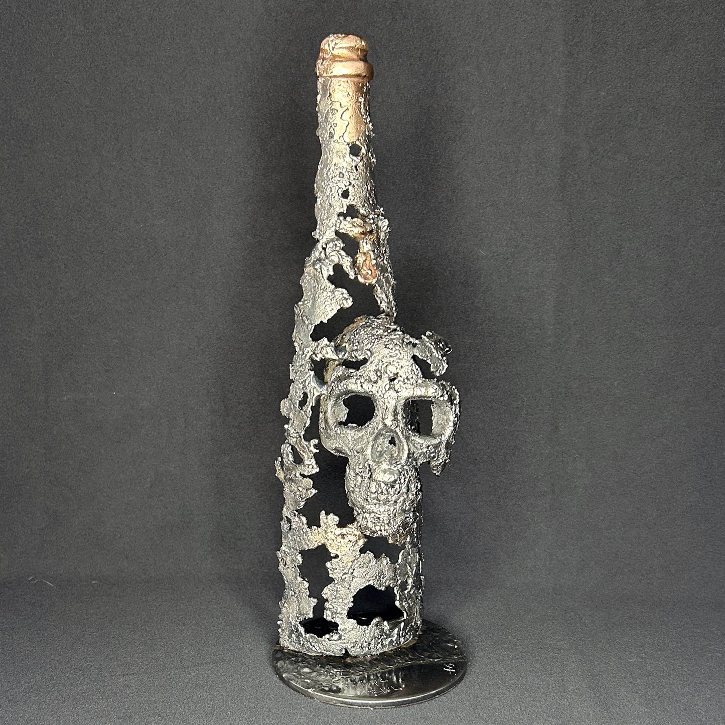 Sculpture en dentelle de métal représentant une tête de mort intégrée à une bouteille de vin, réalisée en acier et bronze par Philippe Buil.