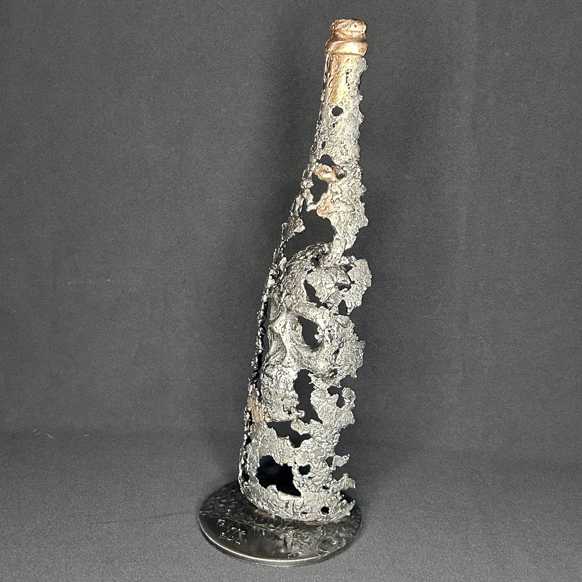 Sculpture en dentelle de métal représentant une tête de mort intégrée à une bouteille de vin, réalisée en acier et bronze par Philippe Buil.