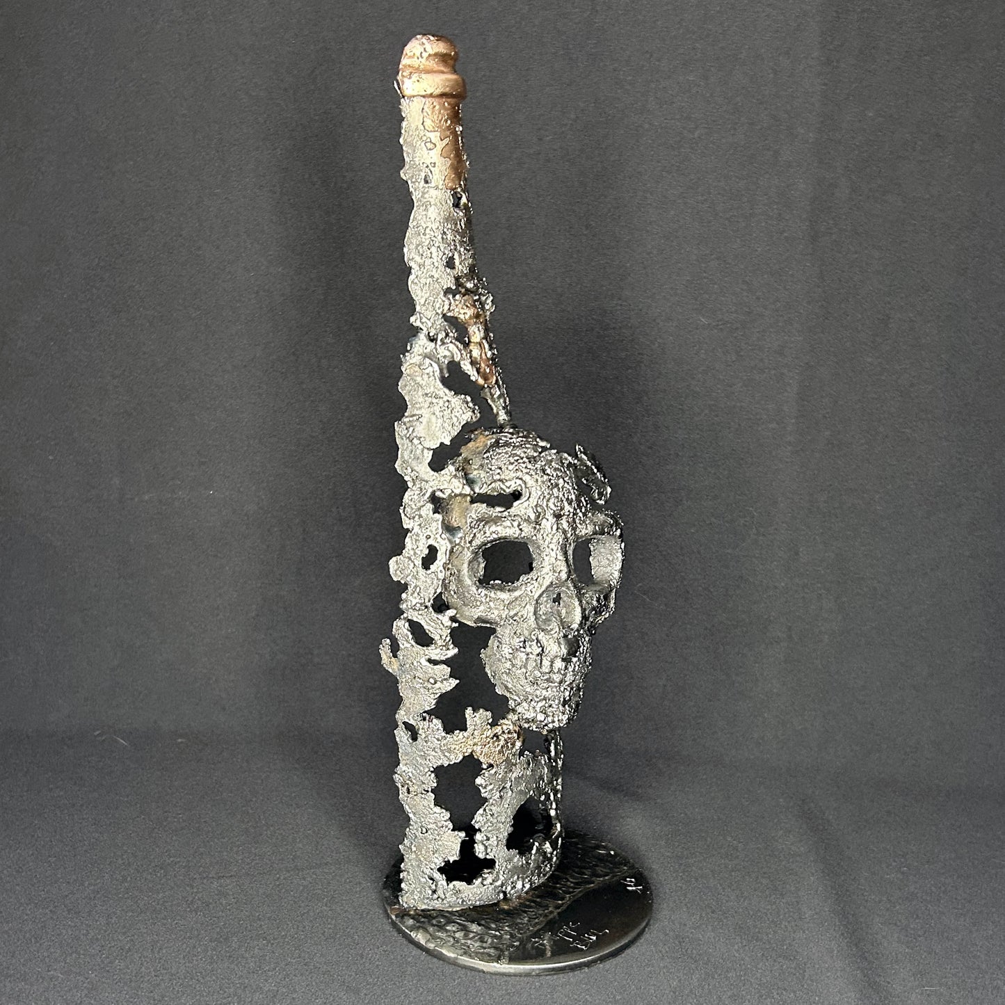 Sculpture en dentelle de métal représentant une tête de mort intégrée à une bouteille de vin, réalisée en acier et bronze par Philippe Buil.