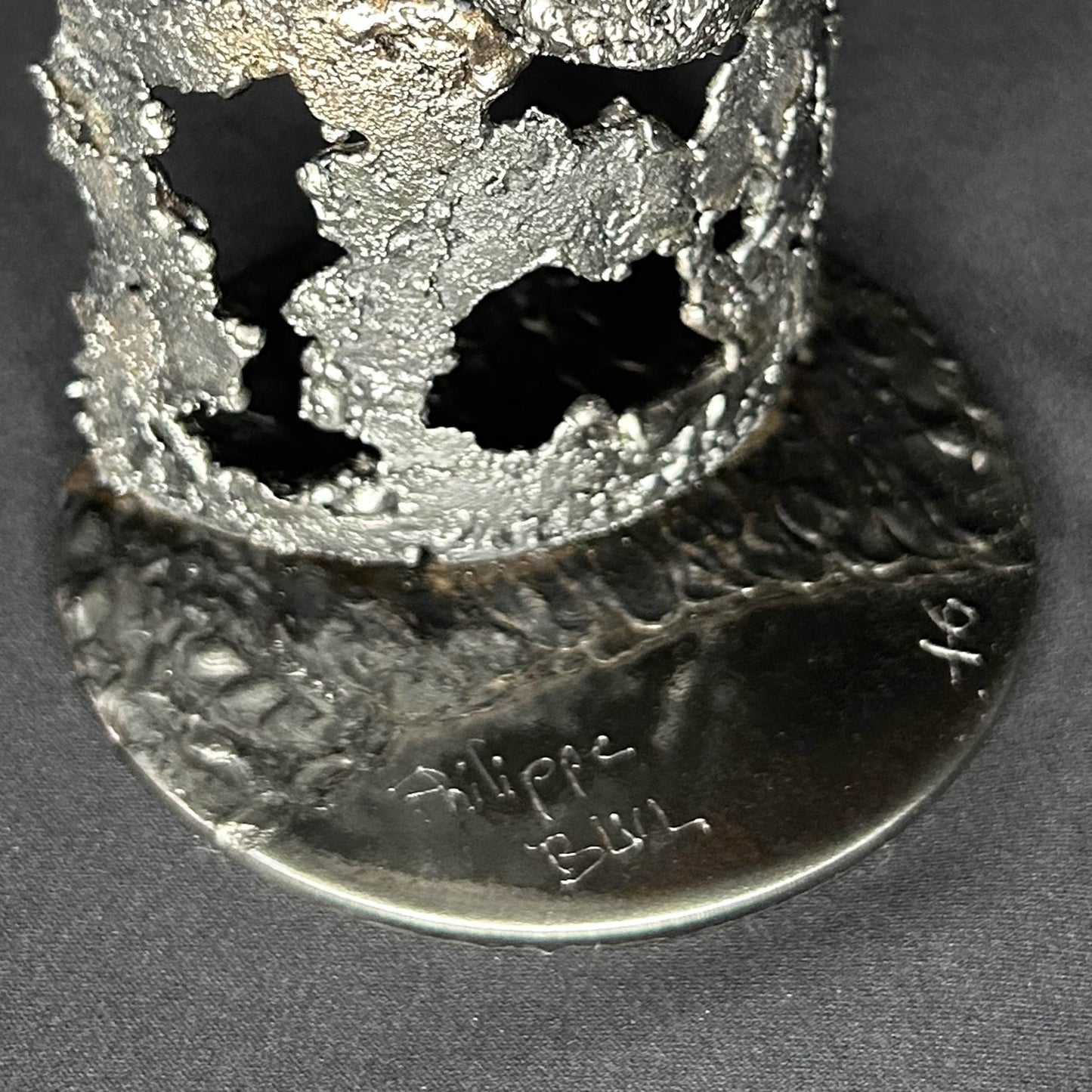 Sculpture en dentelle de métal représentant une tête de mort intégrée à une bouteille de vin, réalisée en acier et bronze par Philippe Buil.