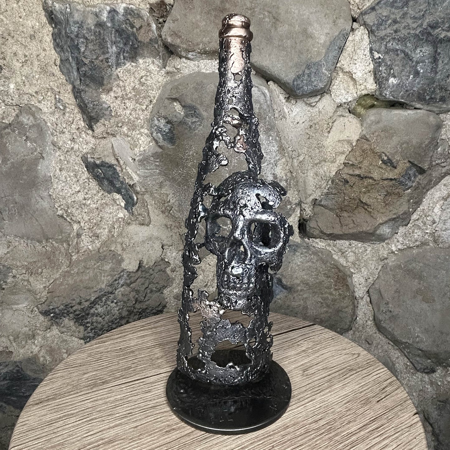 Sculpture en dentelle de métal représentant une tête de mort intégrée à une bouteille de vin, réalisée en acier et bronze par Philippe Buil.