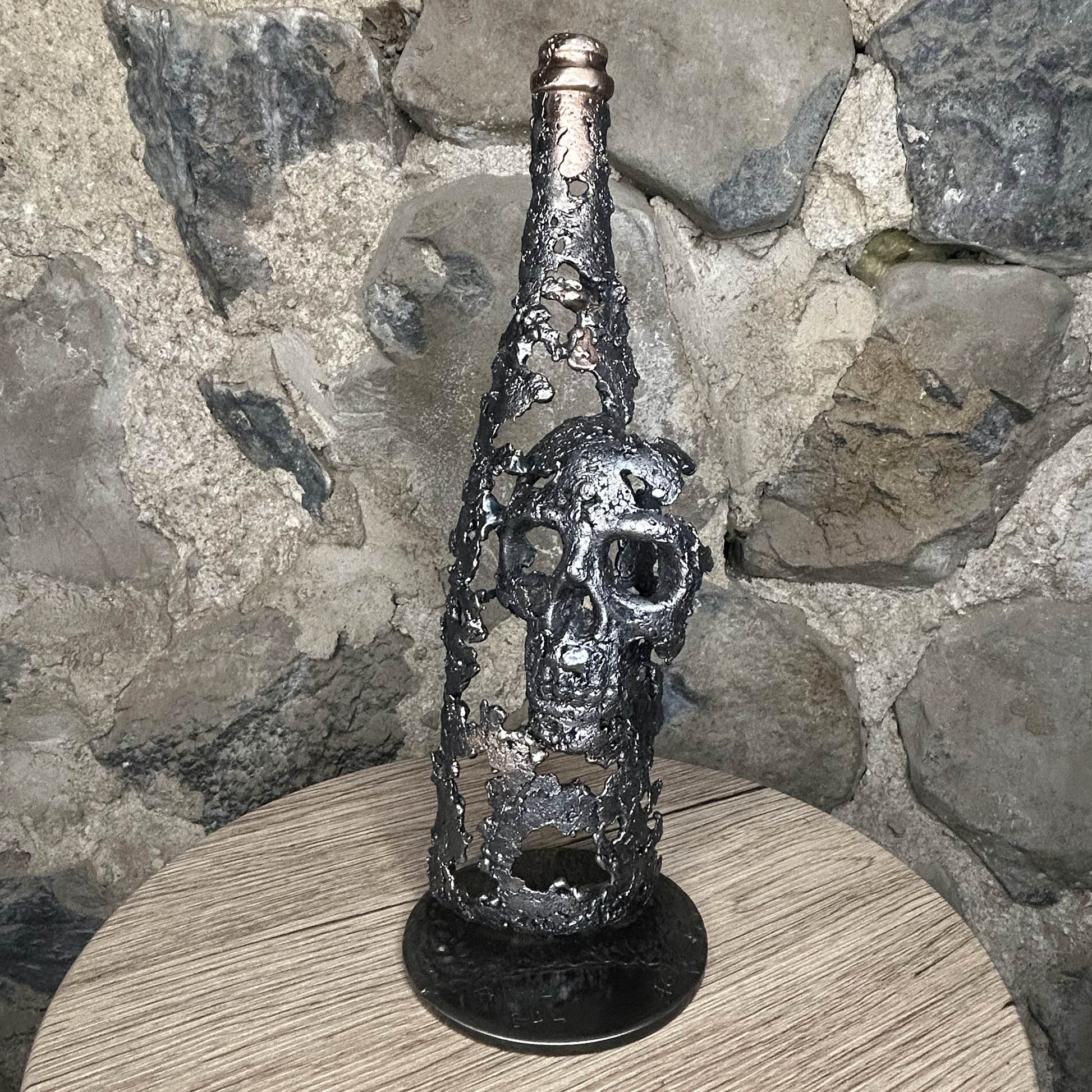 Sculpture en dentelle de métal représentant une tête de mort intégrée à une bouteille de vin, réalisée en acier et bronze par Philippe Buil.