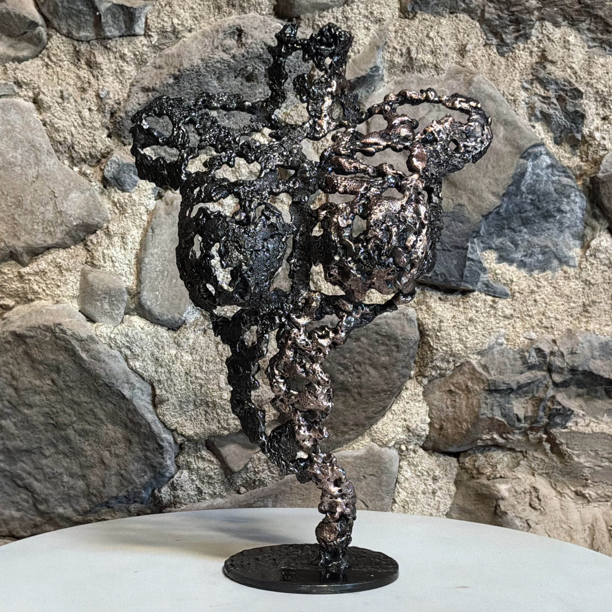 Les Signes de Demain, sculpture féminine en dentelle de métal présentée sur un meuble devant un mur en pierre dans un intérieur chaleureux.