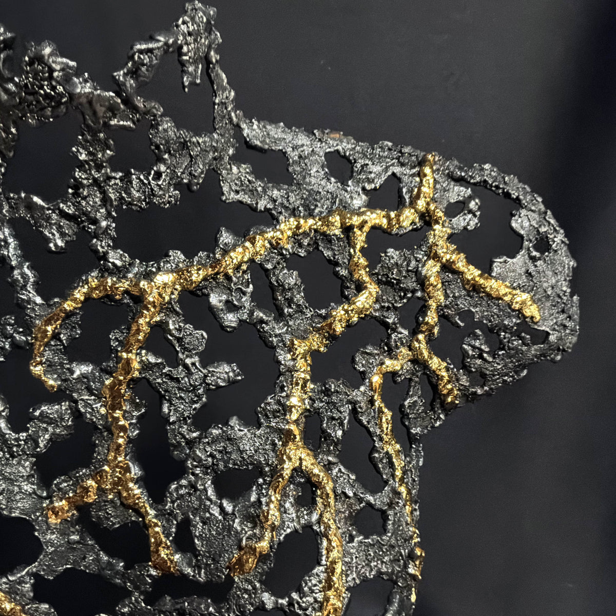 Gros plan sur les lignes dorées appliquées sur la dentelle de métal de la sculpture Belisama