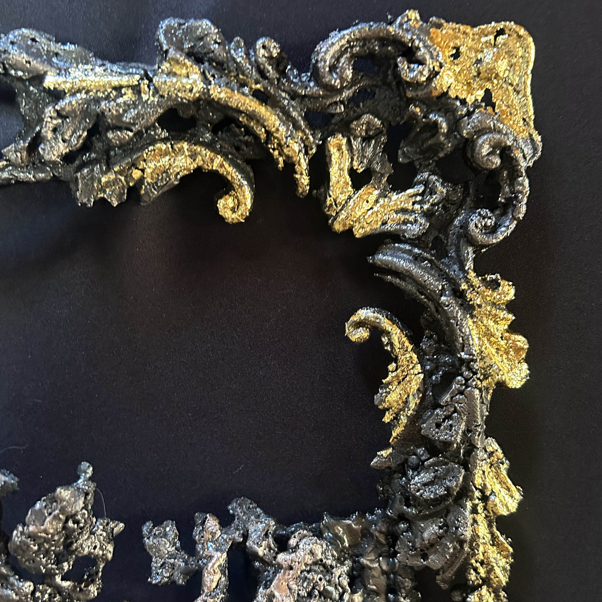 Gros plan sur les feuilles métallisées dorées soulignant les arabesques du cadre sculpté