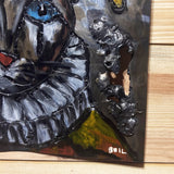 Sculpture murale carrée de 25x25 cm représentant un chat arlequin aux yeux bleus intenses, portant une collerette blanche et un chapeau rayé rouge et jaune. L’œuvre est réalisée en acier texturé et pigments, avec un fond gris brumeux et métallisé