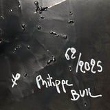 Sculpture murale carrée de 25x25 cm représentant un chat arlequin aux yeux bleus intenses, portant une collerette blanche et un chapeau rayé rouge et jaune. L’œuvre est réalisée en acier texturé et pigments, avec un fond gris brumeux et métallisé