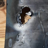 Tableau mural de 25×25 cm représentant un chat à béret dans un décor urbain gris et texturé. L’œuvre est réalisée en métal découpé avec des zones de dentelle de métal et colorée avec des pigments, créant un effet expressif et contrasté.