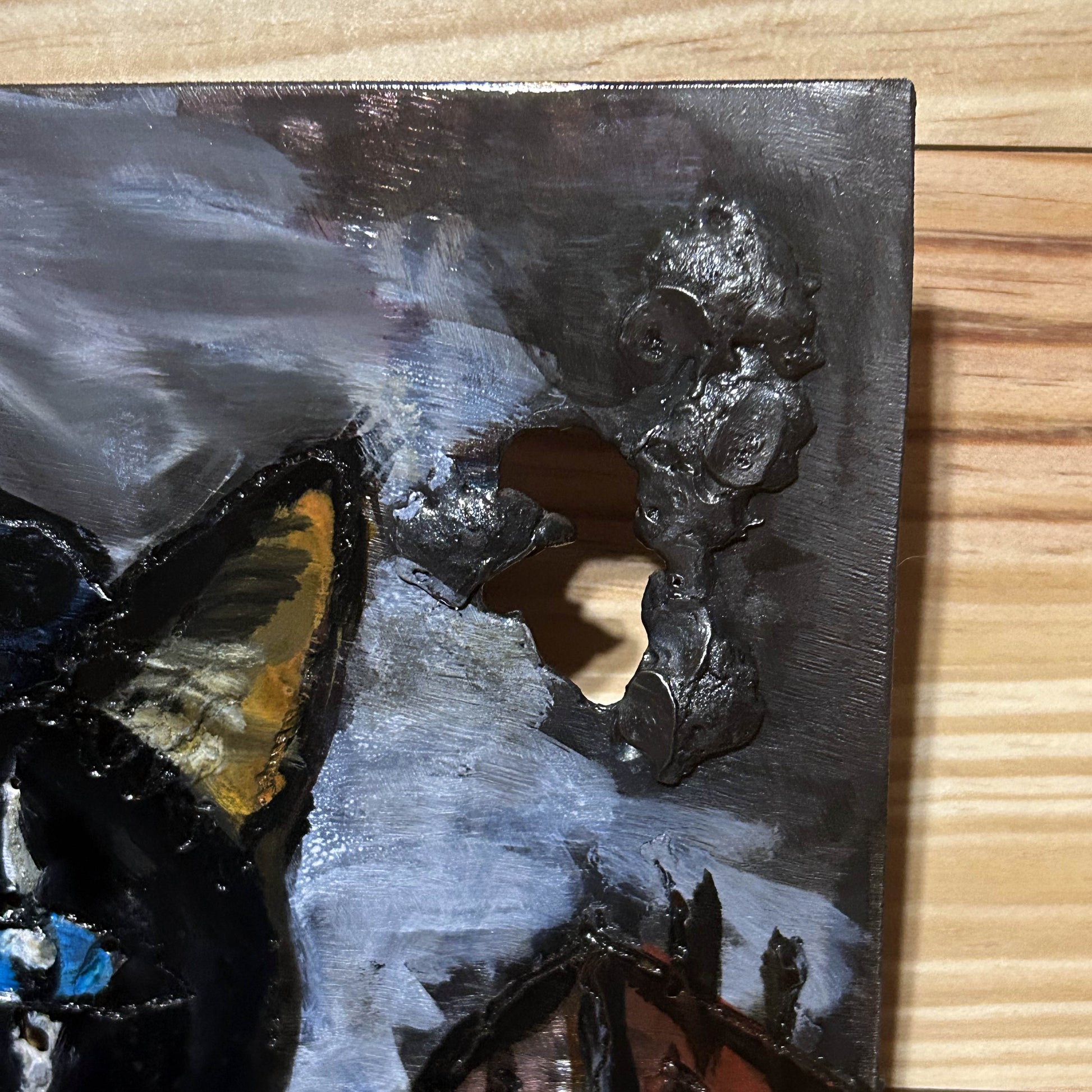 Tableau mural de 25×25 cm représentant un chat à béret dans un décor urbain gris et texturé. L’œuvre est réalisée en métal découpé avec des zones de dentelle de métal et colorée avec des pigments, créant un effet expressif et contrasté.