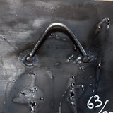 Tableau mural de 25×25 cm représentant un chat à béret dans un décor urbain gris et texturé. L’œuvre est réalisée en métal découpé avec des zones de dentelle de métal et colorée avec des pigments, créant un effet expressif et contrasté.