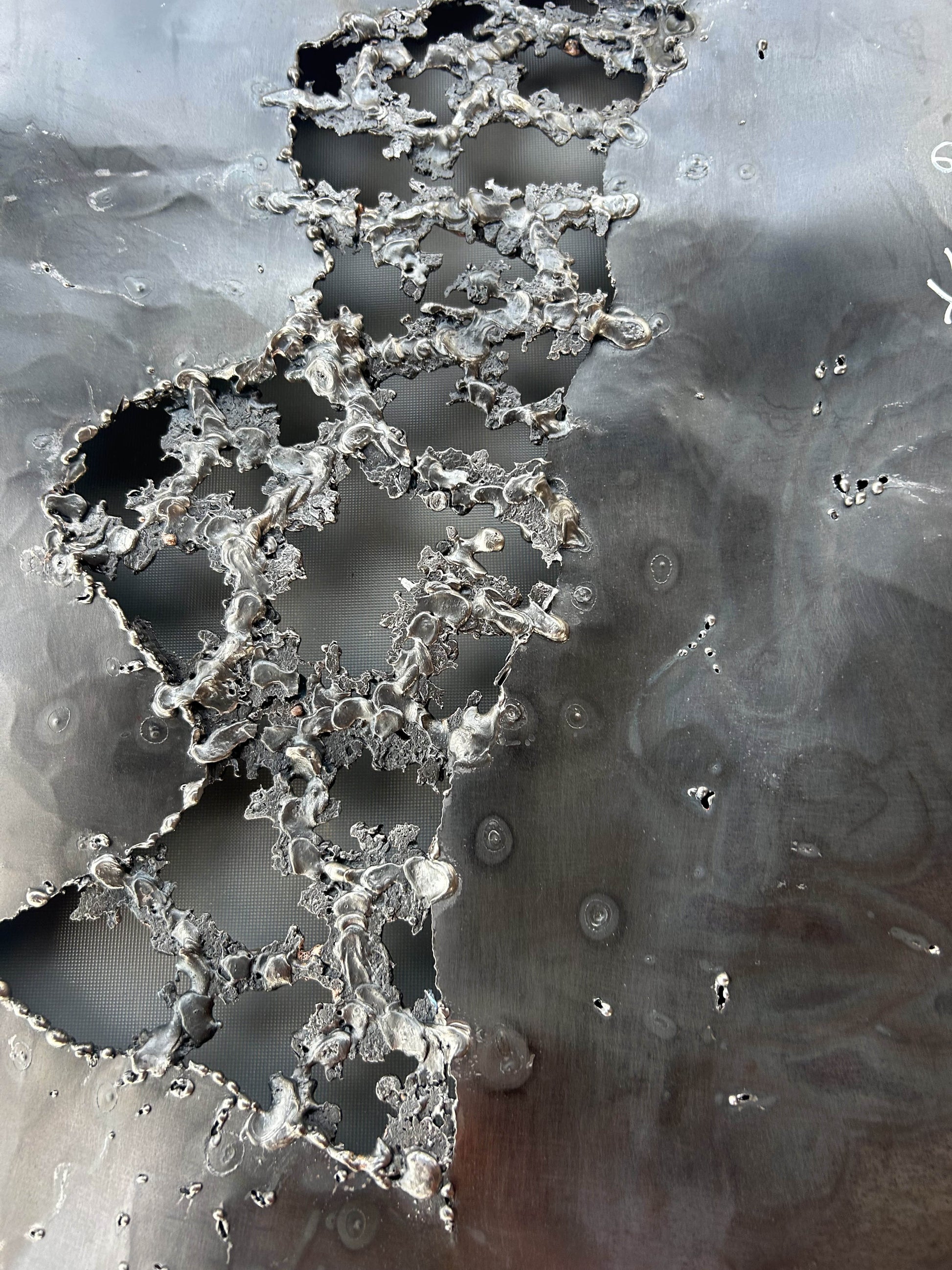 Tableau contemporain en métal de Philippe Buil représentant un visage en relief, moitié peint avec des pigments, moitié ajouré en dentelle d’acier et de bronze, créant un jeu d’ombres et de lumière.