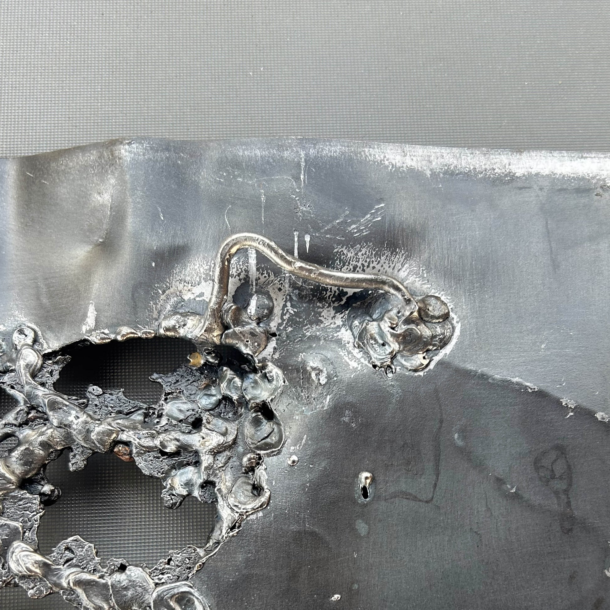 Tableau contemporain en métal de Philippe Buil représentant un visage en relief, moitié peint avec des pigments, moitié ajouré en dentelle d’acier et de bronze, créant un jeu d’ombres et de lumière.