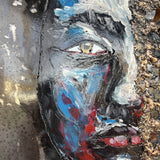 Tableau contemporain en métal de Philippe Buil représentant un visage en relief, moitié peint avec des pigments, moitié ajouré en dentelle d’acier et de bronze, créant un jeu d’ombres et de lumière.