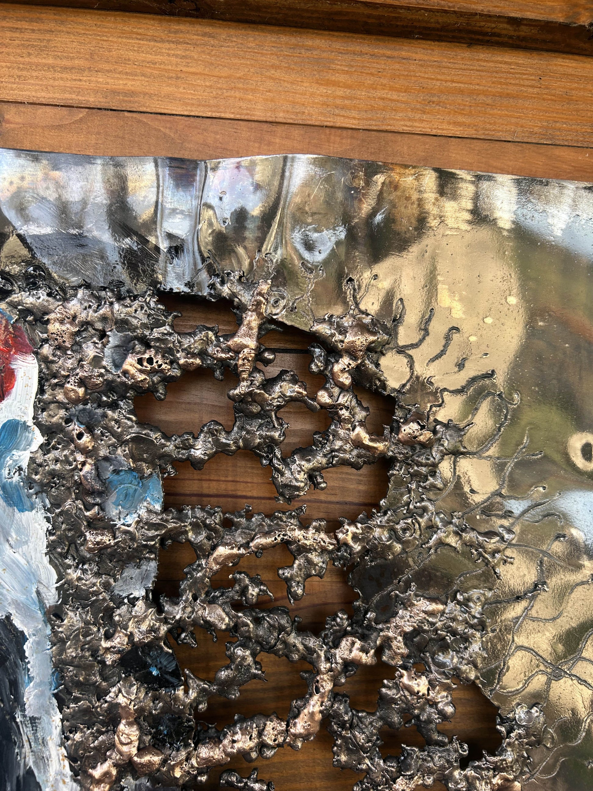 Tableau contemporain en métal de Philippe Buil représentant un visage en relief, moitié peint avec des pigments, moitié ajouré en dentelle d’acier et de bronze, créant un jeu d’ombres et de lumière.