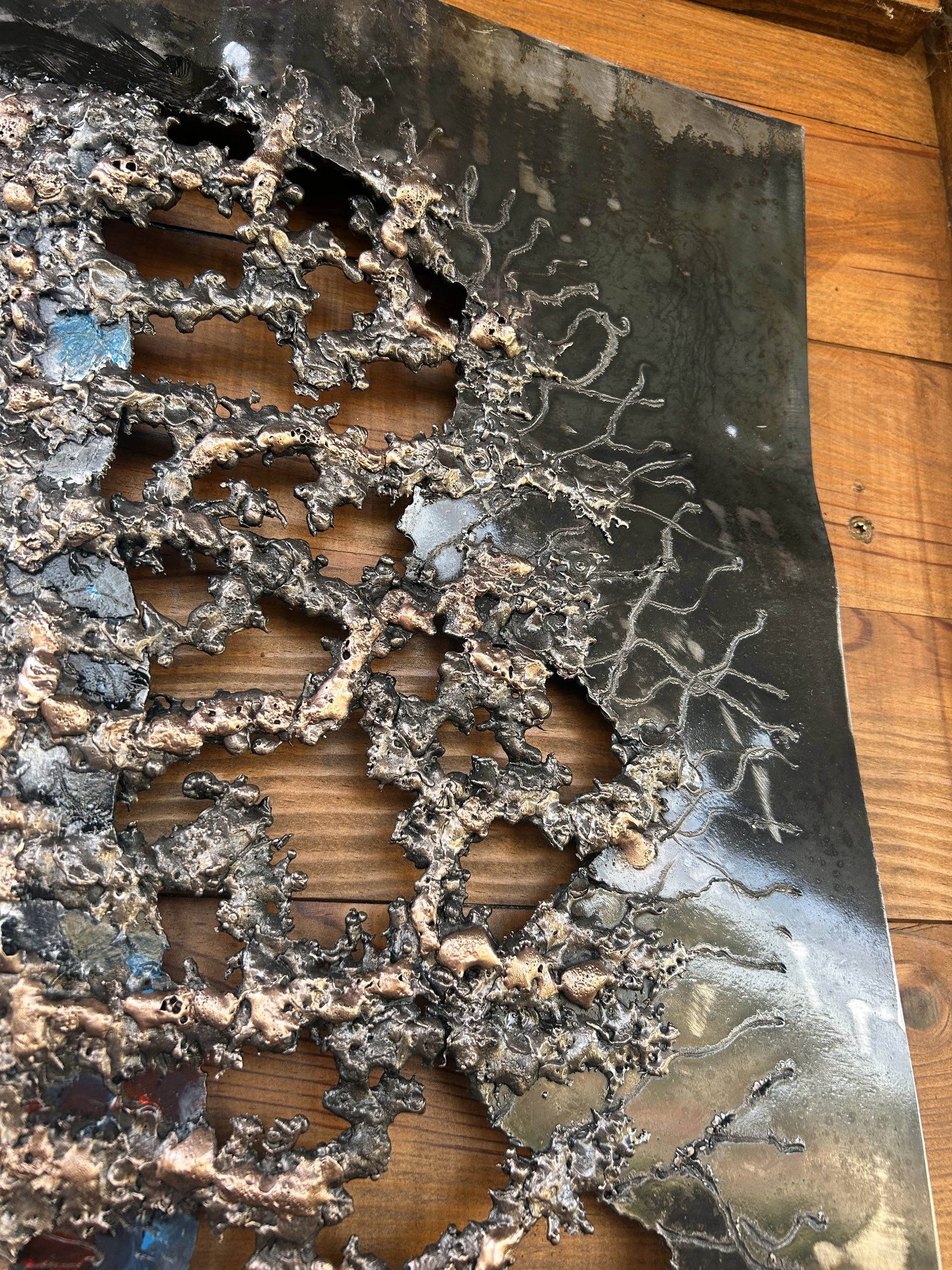 Tableau contemporain en métal de Philippe Buil représentant un visage en relief, moitié peint avec des pigments, moitié ajouré en dentelle d’acier et de bronze, créant un jeu d’ombres et de lumière.