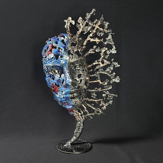 Sculpture de Philippe Buil représentant un visage humain en dentelle d'acier et bronze. Le côté gauche du visage est coloré avec des pigments bleus et rouges, tandis que le côté droit se transforme en une structure métallique ajourée et arborescente.