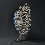 Sculpture de Philippe Buil représentant un visage humain en dentelle d'acier et bronze. Le côté gauche du visage est coloré avec des pigments bleus et rouges, tandis que le côté droit se transforme en une structure métallique ajourée et arborescente.