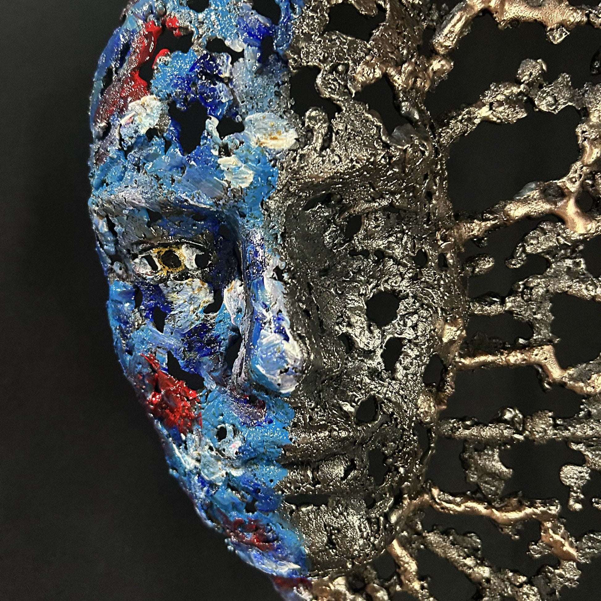 Sculpture de Philippe Buil représentant un visage humain en dentelle d'acier et bronze. Le côté gauche du visage est coloré avec des pigments bleus et rouges, tandis que le côté droit se transforme en une structure métallique ajourée et arborescente.