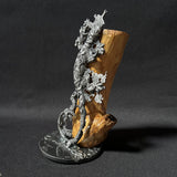 Sculpture contemporaine représentant une salamandre en dentelle de métal (acier), fixée sur un socle métallique circulaire et appuyée contre un morceau de bois naturel, œuvre de Philippe Buil, sur fond sombre.